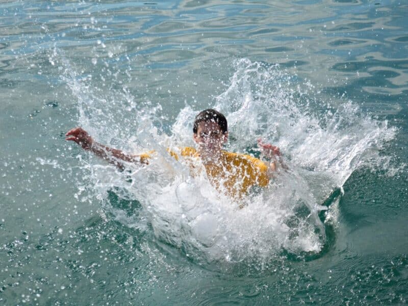 Boy just jumped into water and it has splashed all around him